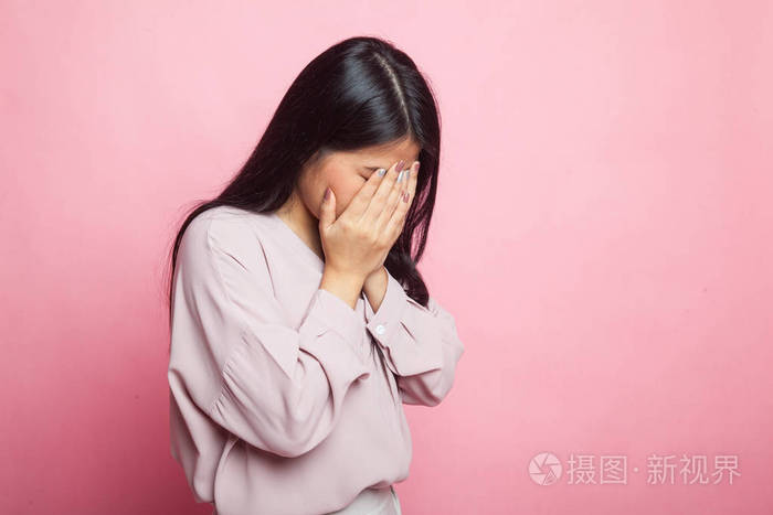 悲伤的年轻亚洲女人用手掌对着粉红色的背景哭泣