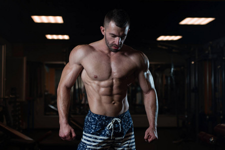一个肌肉发达的野蛮运动员在健身房摆姿势炫耀他的肌肉。 健康生活方式的概念