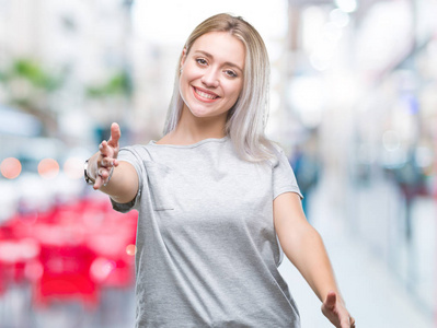 年轻的金发女人在孤立的背景下，看着相机，张开双臂拥抱微笑。拥抱幸福的快乐表情。