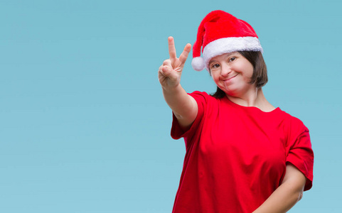 患有唐氏综合症的年轻成年女性戴着圣诞帽，在孤立的背景上微笑，快乐的脸对着镜头眨眼，做胜利标志。第二名。