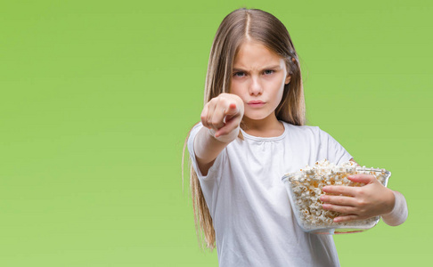年轻漂亮的女孩吃爆米花零食，用手指指向相机和你，手势，正面积极和自信的手势。