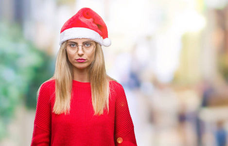 年轻漂亮的金发女人戴着圣诞帽，在孤立的背景上，脸上有着严肃的表情。 简单自然地看着相机。