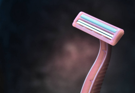 一种粉红色的剃须刀，用于在黑暗的混凝土墙上脱毛。