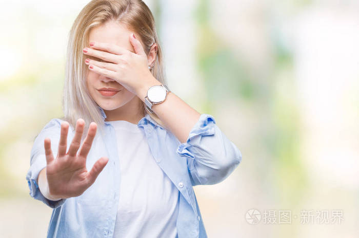 年轻的金发女人在孤立的背景上用手遮住眼睛,用悲伤和恐惧的表情做