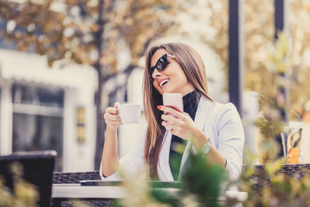快乐的企业家在街上的咖啡店里用手机和笔记本电脑工作，喝咖啡。女孩浏览互联网聊天博客。
