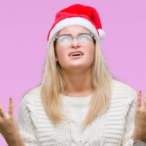 年轻的高加索女人戴着圣诞帽，在孤立的背景上疯狂疯狂地大喊大叫，咄咄逼人的表情和手臂抬起。 挫折概念。