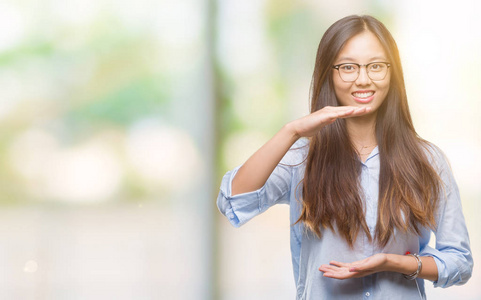 年轻的亚洲商界女性戴着眼镜，在孤立的背景上做手势，双手显示大尺寸的标志符号。 微笑着看着相机。 测量概念。