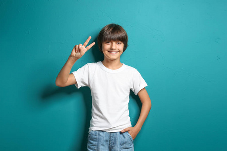 微笑的小男孩穿着t恤，在彩色背景下显示胜利的手势