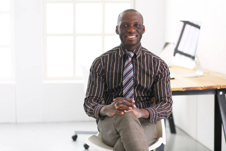 在经典西装的英俊非裔美国商人是使用一台笔记本电脑和微笑在办公室工作的时候