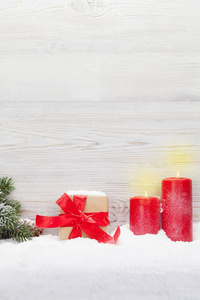圣诞礼品盒蜡烛和杉树枝被雪覆盖在木墙前。 查看复制空间