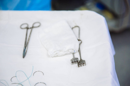 手术时在诊所的医疗桌上做手术器械的特写。金属无菌剪刀夹子手术针在桌上或医生手上。健康的概念, 工具