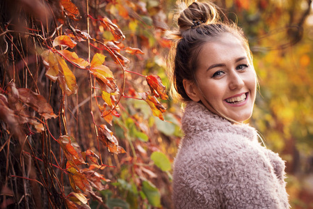 一个美丽的城市女孩在街上的肖像，有秋天的树叶背景。 她是一个快乐的微笑和积极的年轻女人。