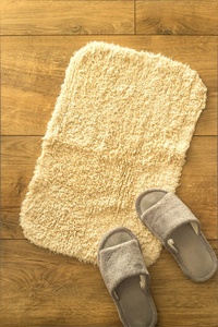 木制地板上有舒适的灰色家庭拖鞋的小特里柔软的米色地毯。 家庭舒适配件的概念。 俯视图平躺