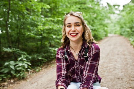 一个美丽的金发女孩的肖像，穿着格子衬衫坐在农村的地上。