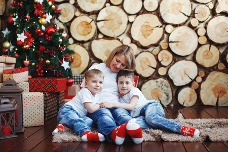 母亲和两个戴着圣诞帽的男孩正坐在新年树旁边，背景是砍树。