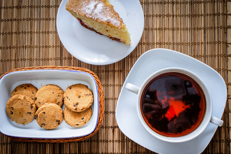 梅饼干蛋糕，一杯热茶，放在稻草床上用品上，篮子里放着巧克力饼干
