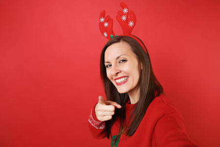 特写自拍的微笑圣诞老人女孩在有趣的装饰鹿角手指在相机上隔离在红色背景。 新年快乐，2019年庆祝节日聚会的理念。 模拟复制空间