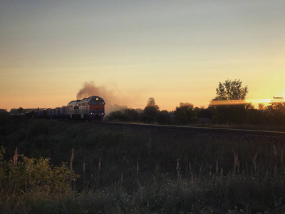 日出时火车在铁路上运行低速载货列车.模糊的通勤列车。火车站顶着阳光明媚的早晨。农村工业景观。