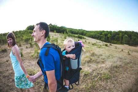 s hand. A man carries his son in a backpack. Walk with the famil