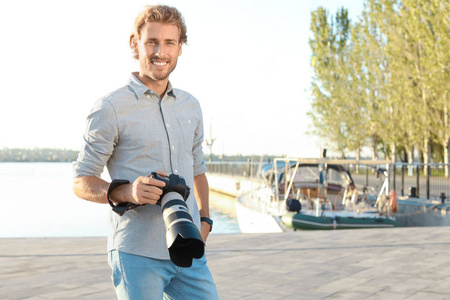英俊的男性摄影师拿着专业的相机在码头。 文本空间