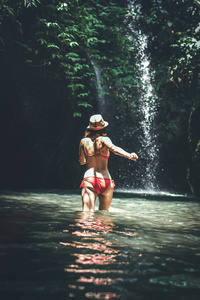 后视图的年轻妇女游客在河里奔跑, 在深丛林与瀑布。真正的冒险概念。巴厘岛