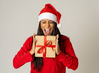 年轻快乐的女人穿着红色毛衣和帽子，看上去很兴奋，展示圣诞礼物回收纸，在圣诞节假日灰色背景下，购物快乐庆祝销售理念。