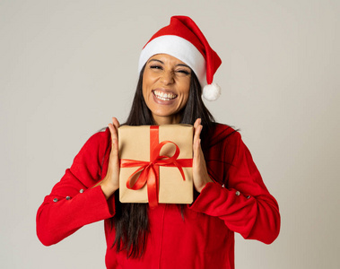 年轻快乐的女人穿着红色毛衣和帽子，看上去很兴奋，展示圣诞礼物回收纸，在圣诞节假日灰色背景下，购物快乐庆祝销售理念。
