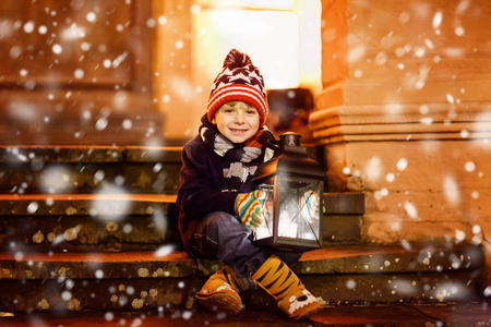 可爱小孩男孩与光的灯笼在教堂附近的楼梯上。在德国的圣诞市场上快乐的孩子。孩子家长在寒冷的冬天里等待