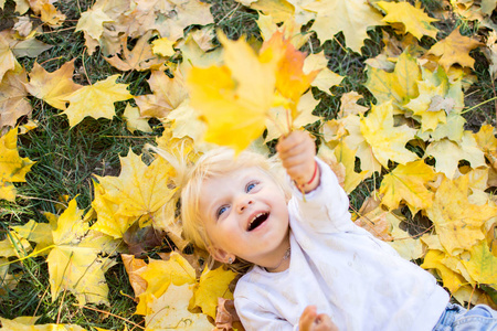 一个蓝眼睛的小女孩躺在落叶上，在一个秋日的晴天快乐地玩耍