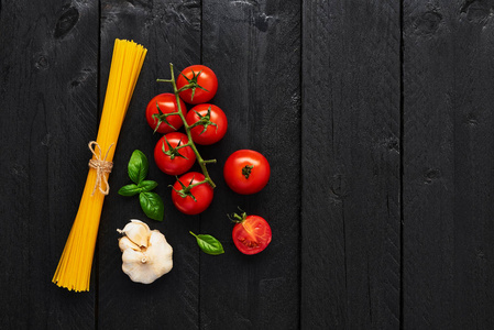 意大利美味菜肴的食物背景，包括意大利面番茄大蒜和罗勒。黑色木桌上各种烹饪原料..顶部视图与复制空间。