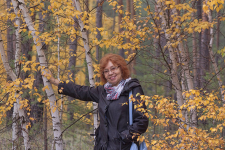 一个成熟的女人在森林里，旁边是一棵黄叶的桦树。 十月秋