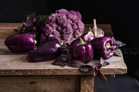 新鲜蔬菜。 深紫辣椒花椰菜，叶罗勒和大蒜在旧的乡村木桌上的黑色背景