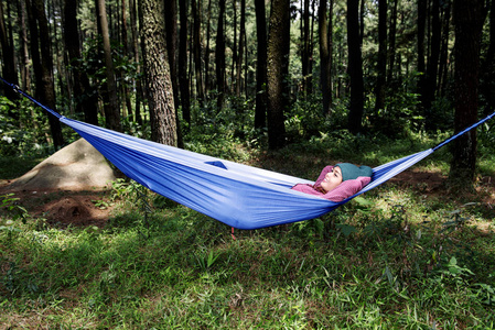 快乐的亚洲旅行者女人在森林的吊床上放松