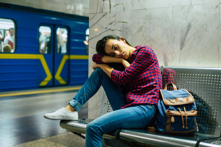 睡眼的年轻女子坐在地下车站的金属长凳上