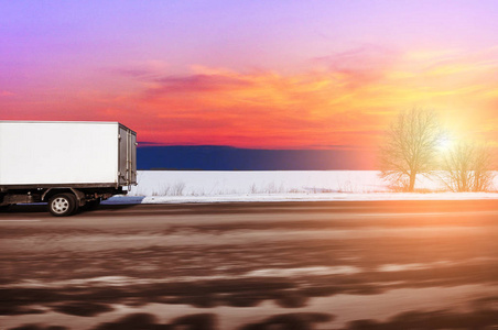 白色卡车箱快速行驶在乡村的冬季道路上，雪与天空，日落