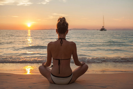 女人在日落海滩上练习瑜伽和冥想莲花的姿势
