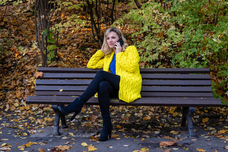 年轻漂亮的金发女人坐在公园的长凳上打电话。