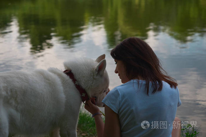微笑的女人和她的狗说话,在水边休息时摸着他的脸