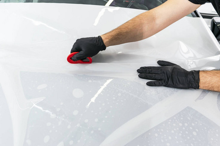 汽车包装专家把乙烯基箔或薄膜放在汽车上。 汽车上的保护膜。 用工具在汽车上涂上保护膜。 汽车细节。 透明薄膜。 汽车油漆保护。 