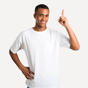 年轻的非裔美国男人在孤立的背景上展示和举起一根手指作为最好的标志