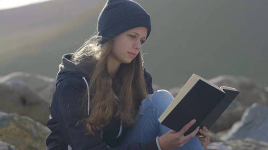 年轻女子坐在岩石上看书