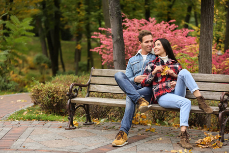 可爱的年轻夫妇坐在秋天公园的木凳上