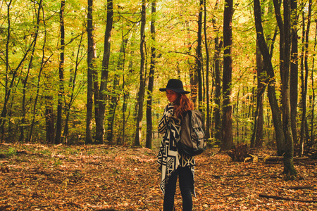 穿着针织民族蓬衫裤和背包的红头发女孩。 大气的变暖是温暖的，太阳在森林里。 自然背景。 女人旅行旅行照片
