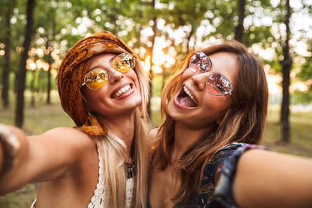 两个快乐的嬉皮士女人在森林里散步时微笑和自拍的照片