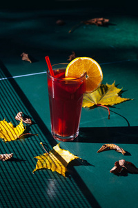 一杯热饮料和绿色网球桌上的秋叶。 在大杯子里涂上葡萄酒，外面有阳光和阴影。