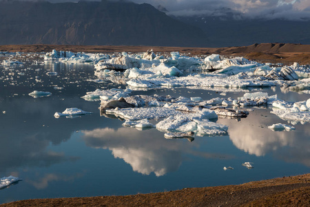 在 Jokulsarlon 冰川泻湖岸边的云雾附近散落融化的冰山, 反射在水中