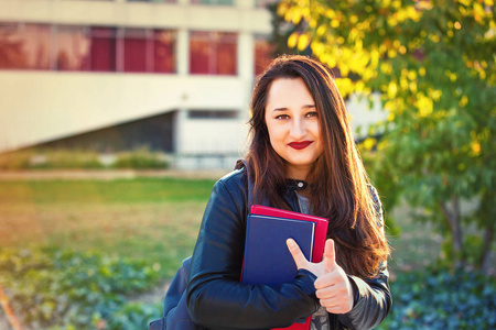 年轻的女学生走在大学校园里，竖起大拇指。