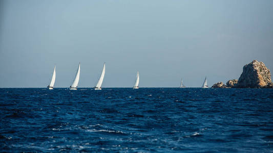 团体游艇船，白色帆近爱琴海的岩石。 帆船比赛。