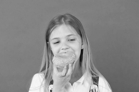 孩子在紫罗兰色背景下吃甜甜圈。小女孩咬着琉璃圈甜甜圈。Candyshop 概念。童年和幸福。垃圾食品的孩子。甜蜜的心情。不健康的