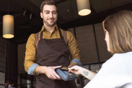 幸福的年轻服务员拿着付款终端，而客户在咖啡馆用信用卡进行非接触购买